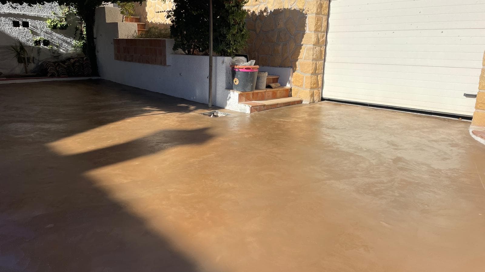 Porche de vivienda con solera de hormigón fratasado fino en tono tostado, junto a la puerta de un garaje.