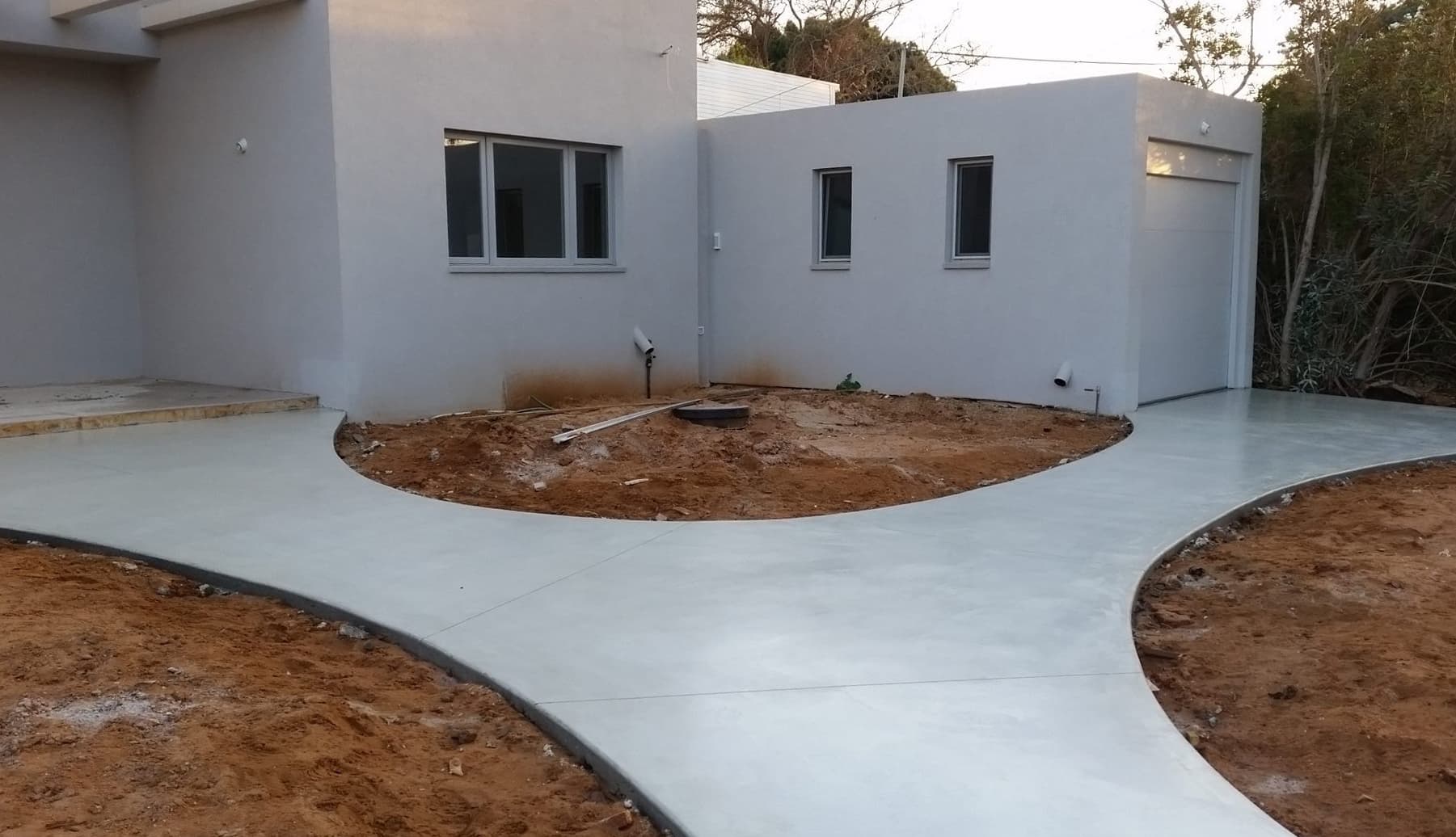 Patio de hormigón pulido gris recién ejecutado ante una vivienda blanca, con el terreno aún sin ajardinar.