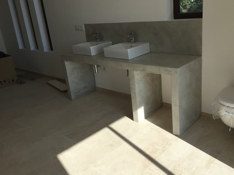 Baño con encimera y frente de microcemento en tono crema, con dos lavabos sobre encimera.