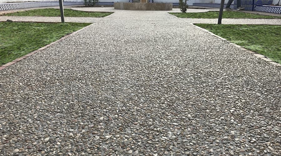 Paseo de hormigón lavado con árido visto gris entre dos franjas de césped.