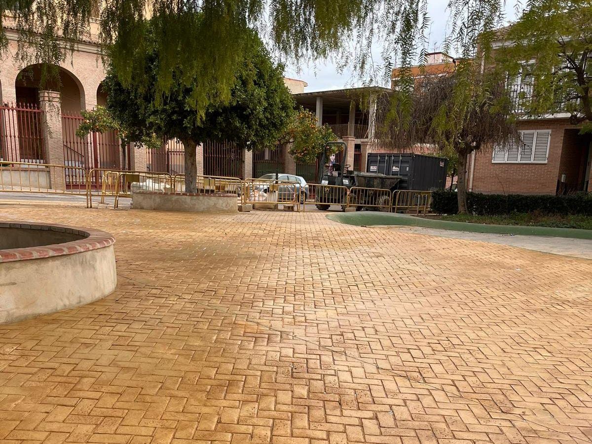 Plaza pavimentada en hormigón impreso con despiece en espiga, con un alcorque circular y arbolado alrededor.