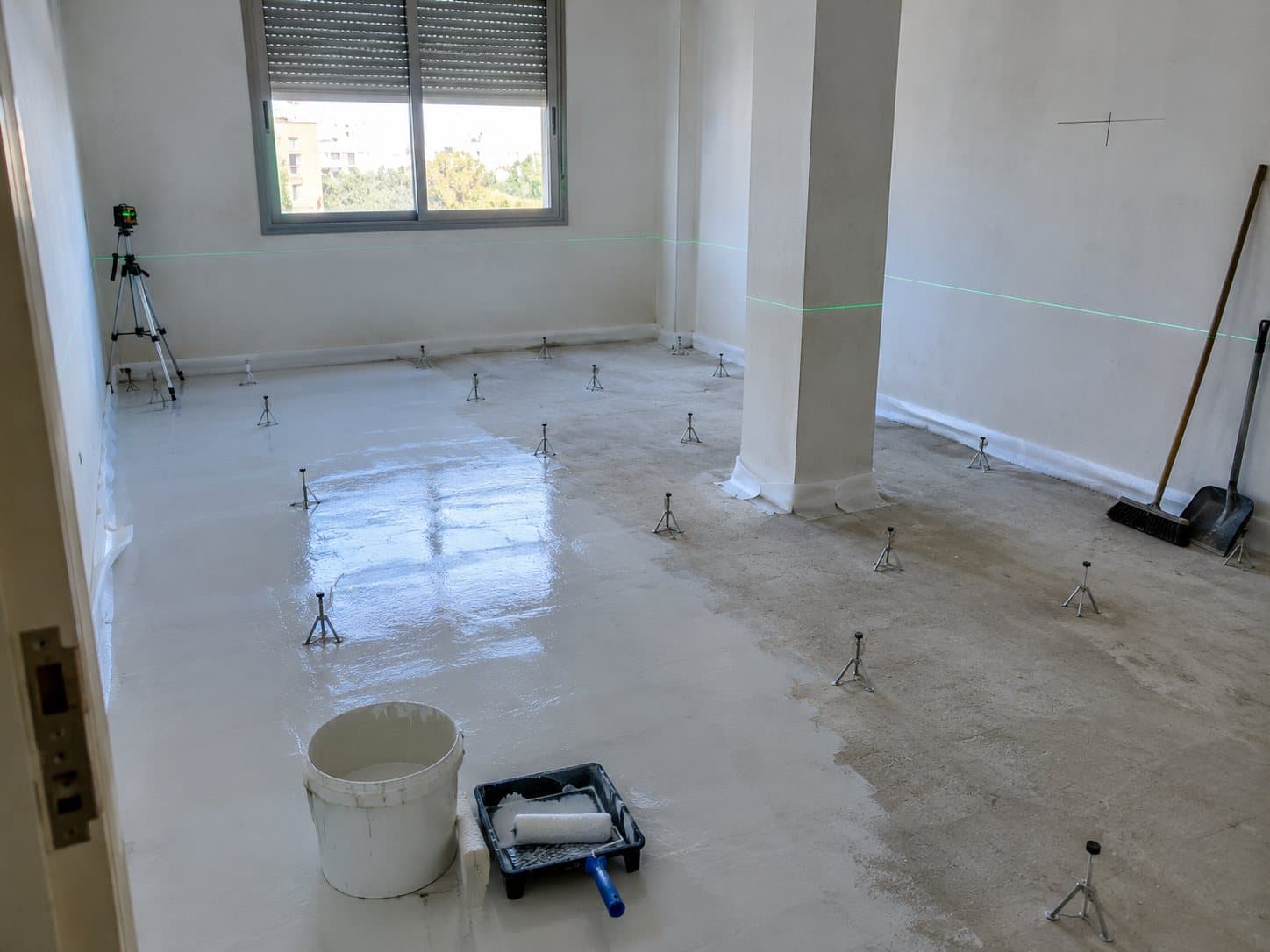 Habitación preparada para el autonivelante: imprimación a medio extender, trípodes de nivelación, banda perimetral y nivel láser.
