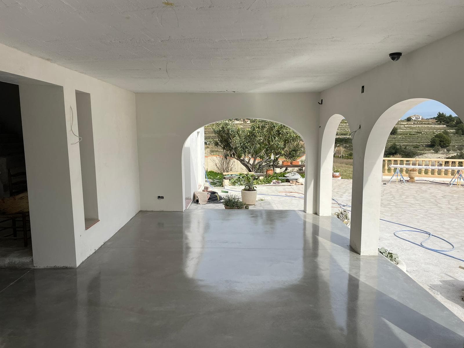 Estancia con arcos y suelo de hormigón pulido continuo que se prolonga hasta el porche.